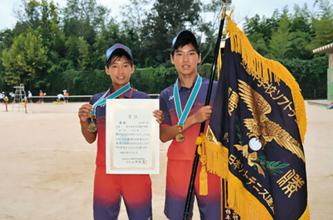少年男子二人がソフトt寝椅子全国中学生ソフトテニス大会の優勝旗を持っている写真