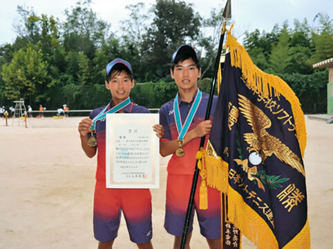 少年男子二人がソフトt寝椅子全国中学生ソフトテニス大会の優勝旗を持っている写真